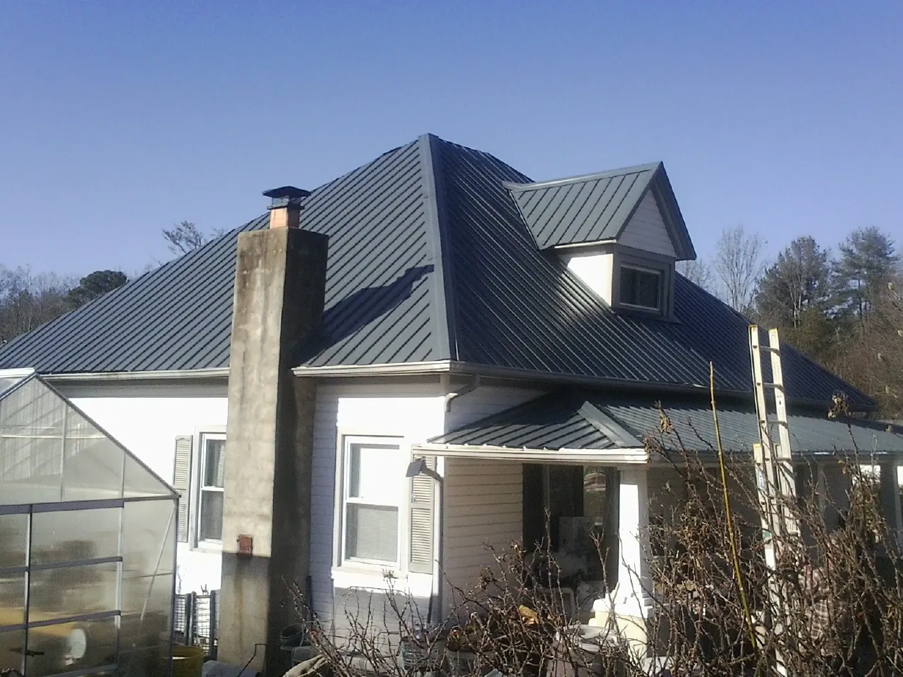Dark blue standing seam metal roof on a white farmhouse with dormer — Slate & Tile Roof Repair by Roofing Brothers in Natural Bridge Station