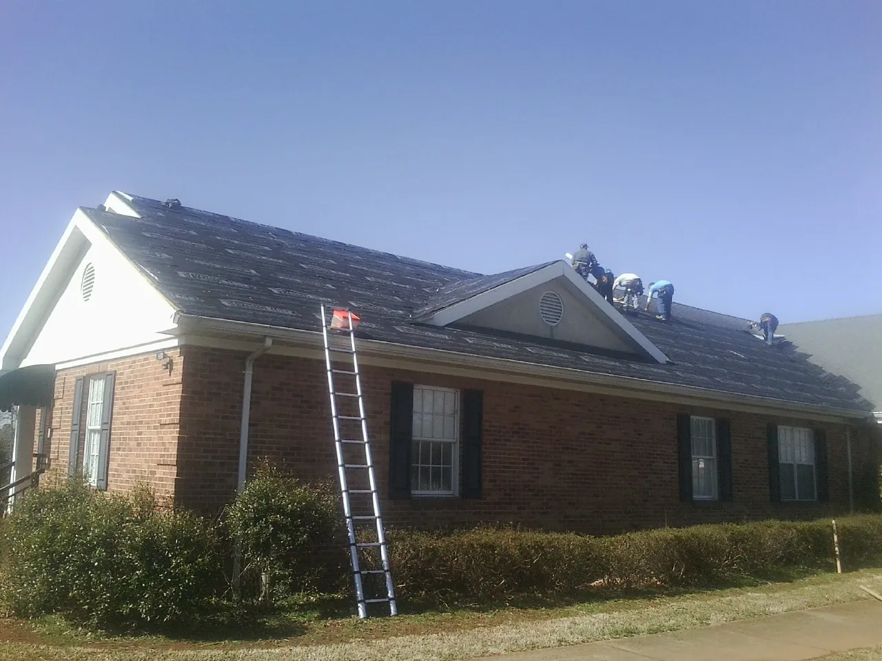 Crew tearing shingles off a brick ranch roof with a ladder set — Emergency Roof Repair work by our crew in Natural Bridge Station