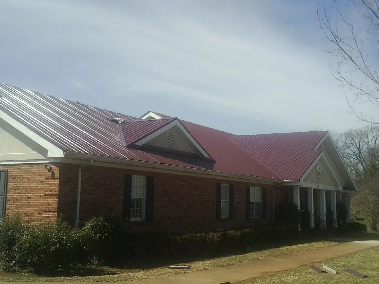 Red metal roof with gabled entries on a long brick building, from a Hail Damage Roof Repair job in Natural Bridge Station