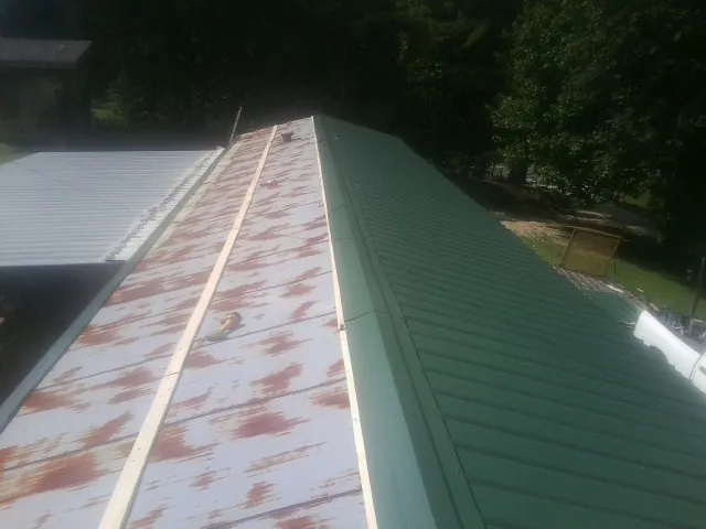 Old rusted panels beside newly installed green metal roofing — Wind Damage Roof Repair by Roofing Brothers in Natural Bridge Station