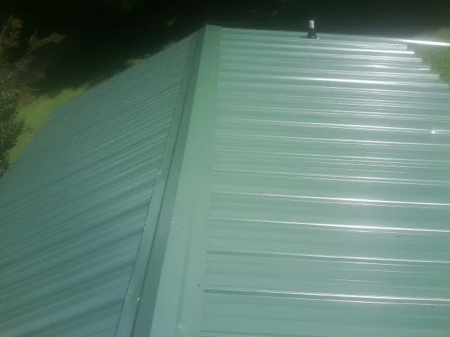 New green metal panels meeting at the ridge of a roof — Flat Roof Repair work by our crew in Natural Bridge Station