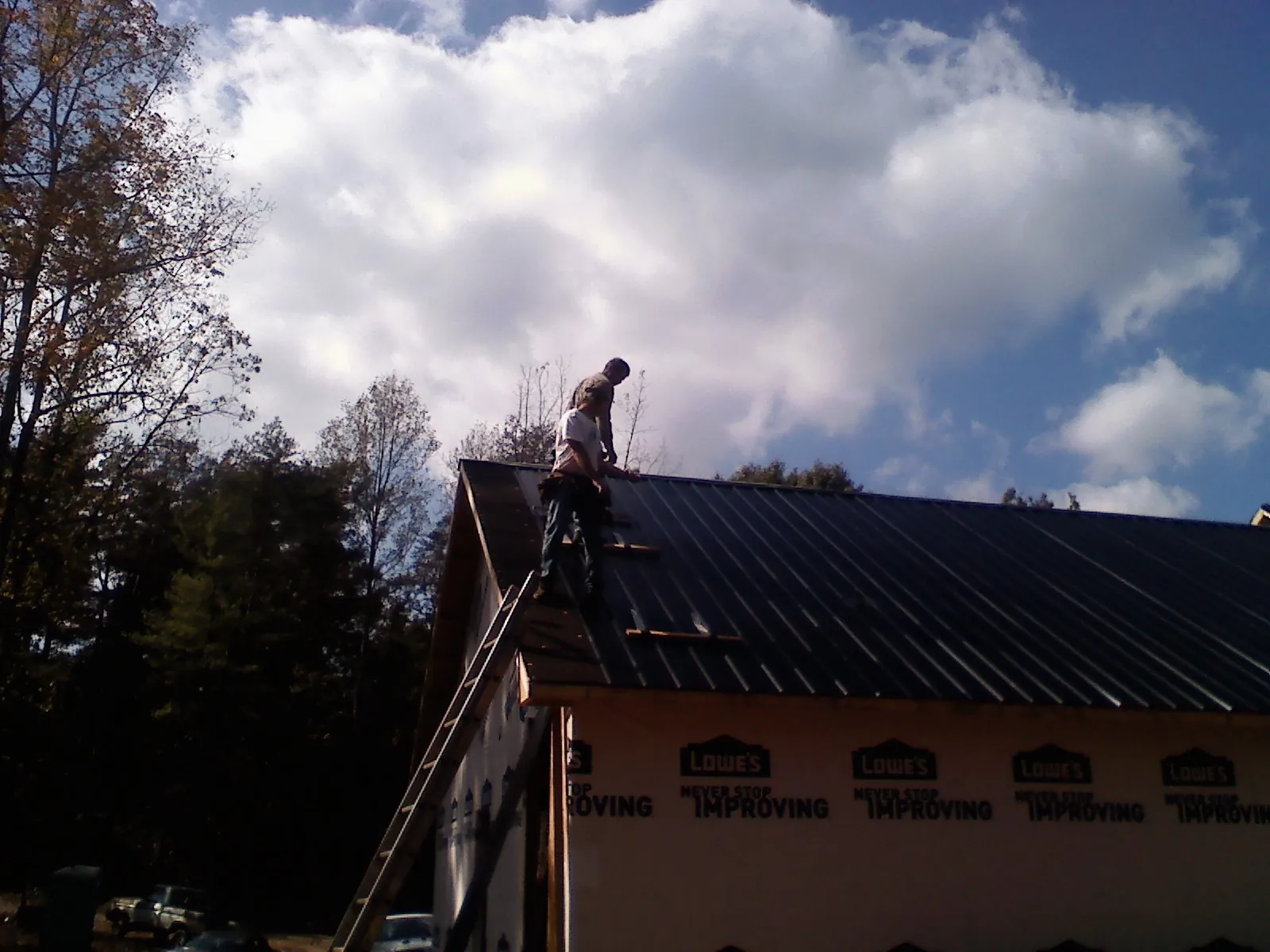 Roofer fastening dark metal panels high against a cloudy sky, from a Roof Inspection job in Natural Bridge Station