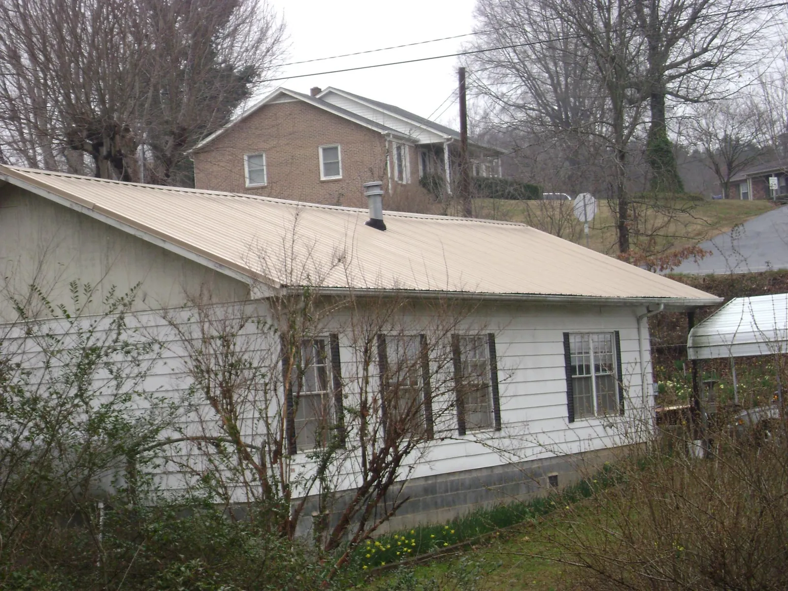 Tan metal roof on a white sided house set into a hillside — Commercial Roofing by Roofing Brothers in Natural Bridge Station